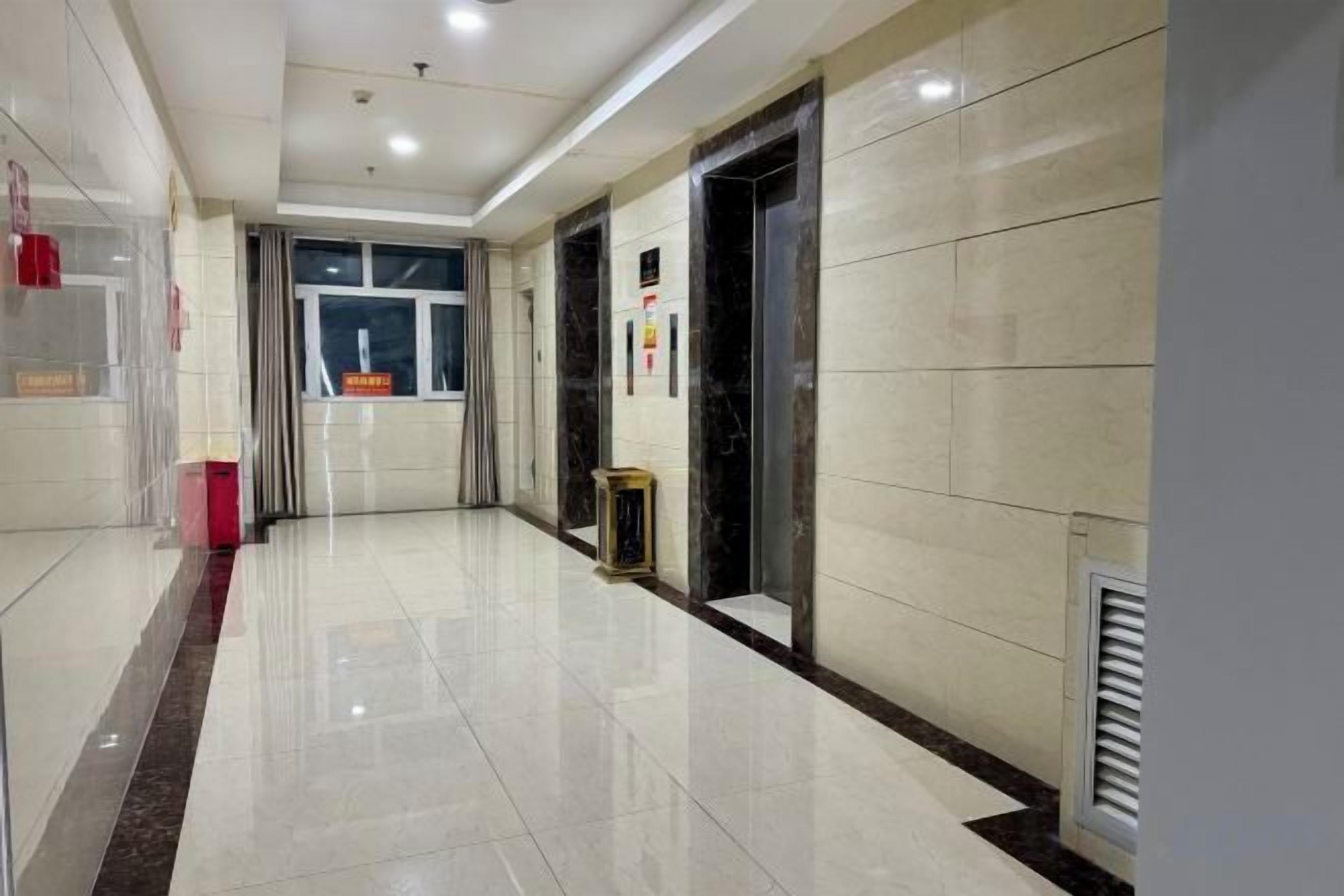 A clean, well-lit hallway with a tiled floor, a trash bin, and a door leading to another room.
