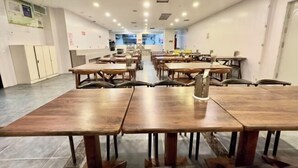 A spacious dining area with multiple wooden tables and chairs, a central aisle, and a view of the kitchen area in the background. - Super 8 Hotel (Qitai Tuanjie South Road Branch) (Qitai)