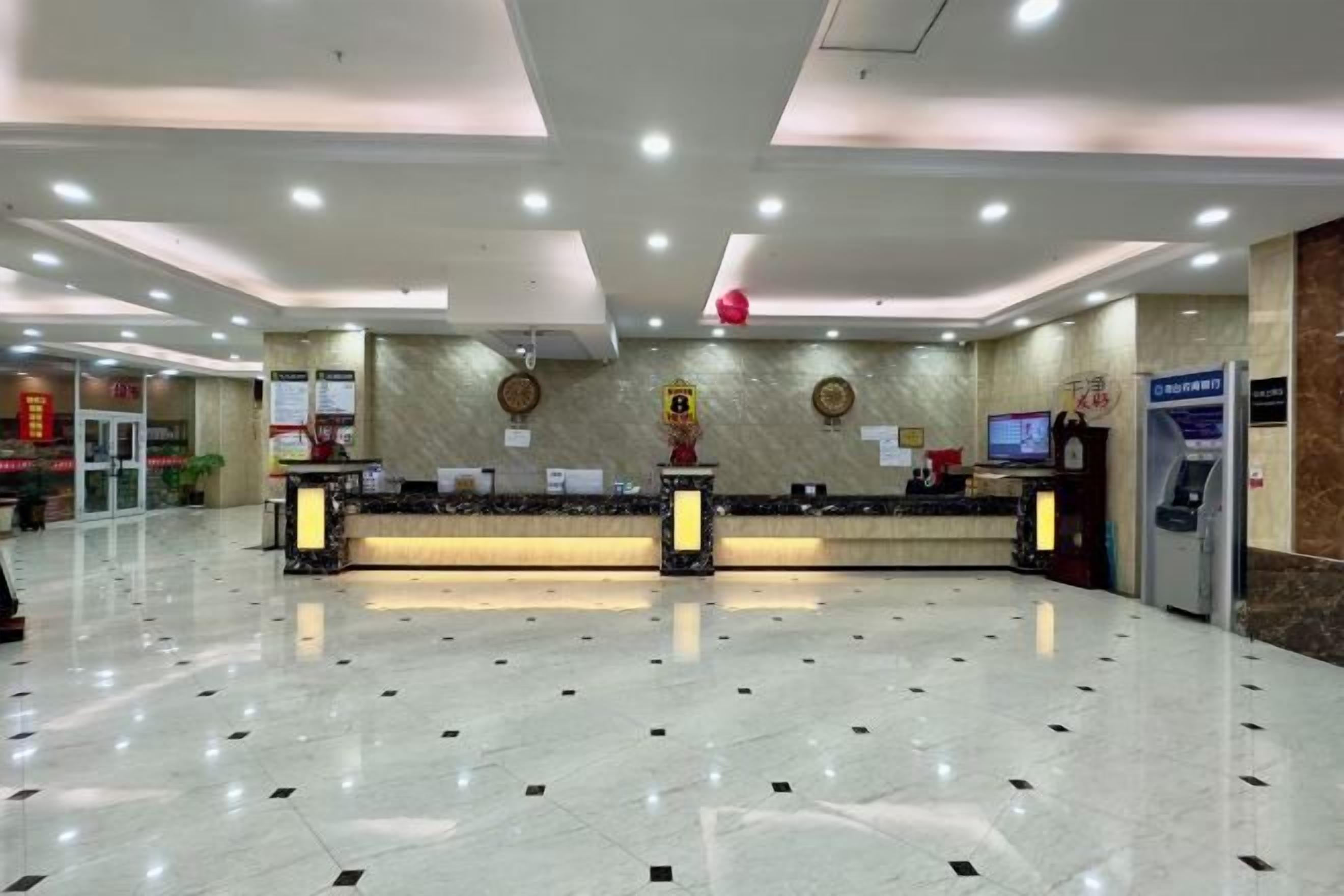 A hotel reception area with a marble floor, two reception desks, a digital screen, and a vending machine.