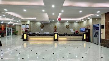 A hotel reception area with a marble floor, two reception desks, a digital screen, and a vending machine.