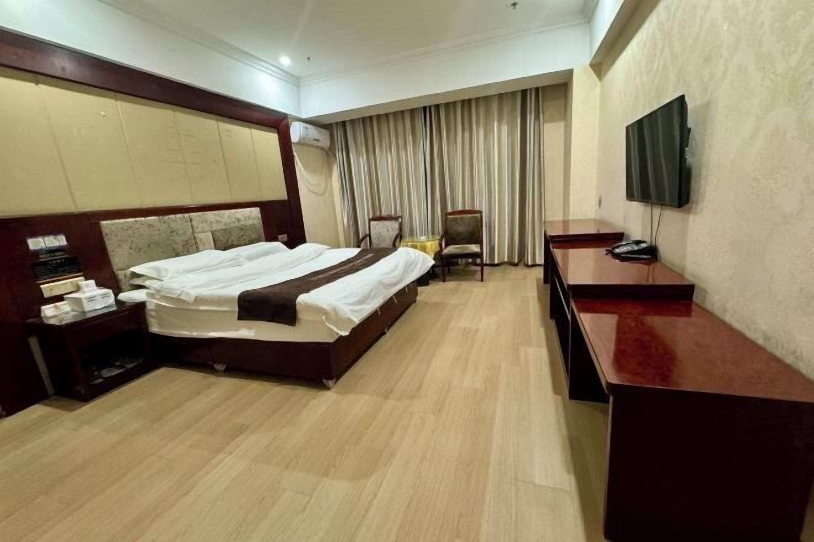 Ein Hotelzimmer mit Bett, Nachttisch, Stuhl, Schreibtisch, Fernseher und Vorhängen.