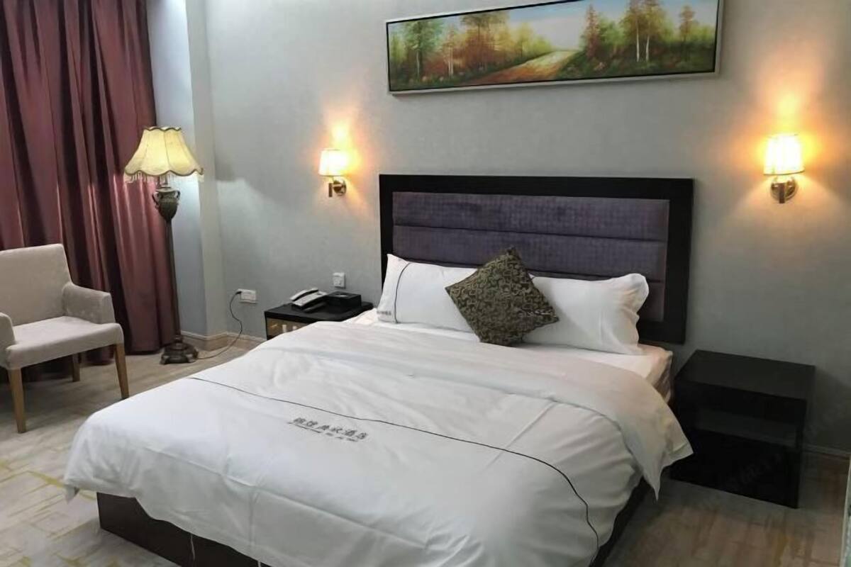 Hotellihuone, jossa on suuri sänky, tuoli, yöpöytä, lamppu ja taulu seinällä.