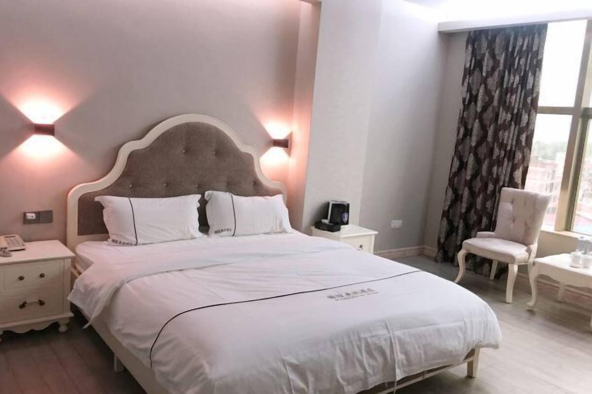 Hotellihuone, jossa on suuri sänky, yöpöydät, tuoli ja ikkuna, jossa on verhot.