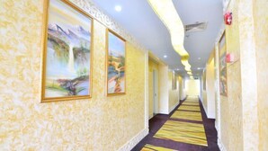 A hotel corridor with a patterned carpet, framed artwork on the walls, and a ceiling with recessed lighting. - Boluo Gengxin Hotel (Boluo)