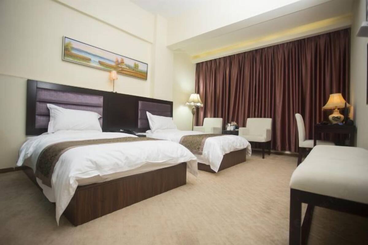 Hotellihuone, jossa on kaksi sänkyä, työpöytä, tuoli ja suuri ikkuna, jossa on verhot.