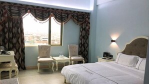 A hotel room with a bed, two chairs, a small table, a nightstand, and a window with curtains. - Boluo Gengxin Hotel (Boluo)