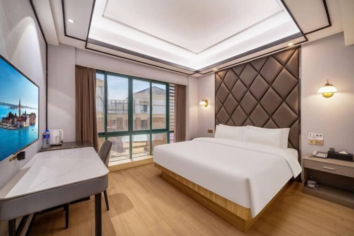 A hotel room with a bed, a desk, a TV, a window with a view, and a ceiling light.