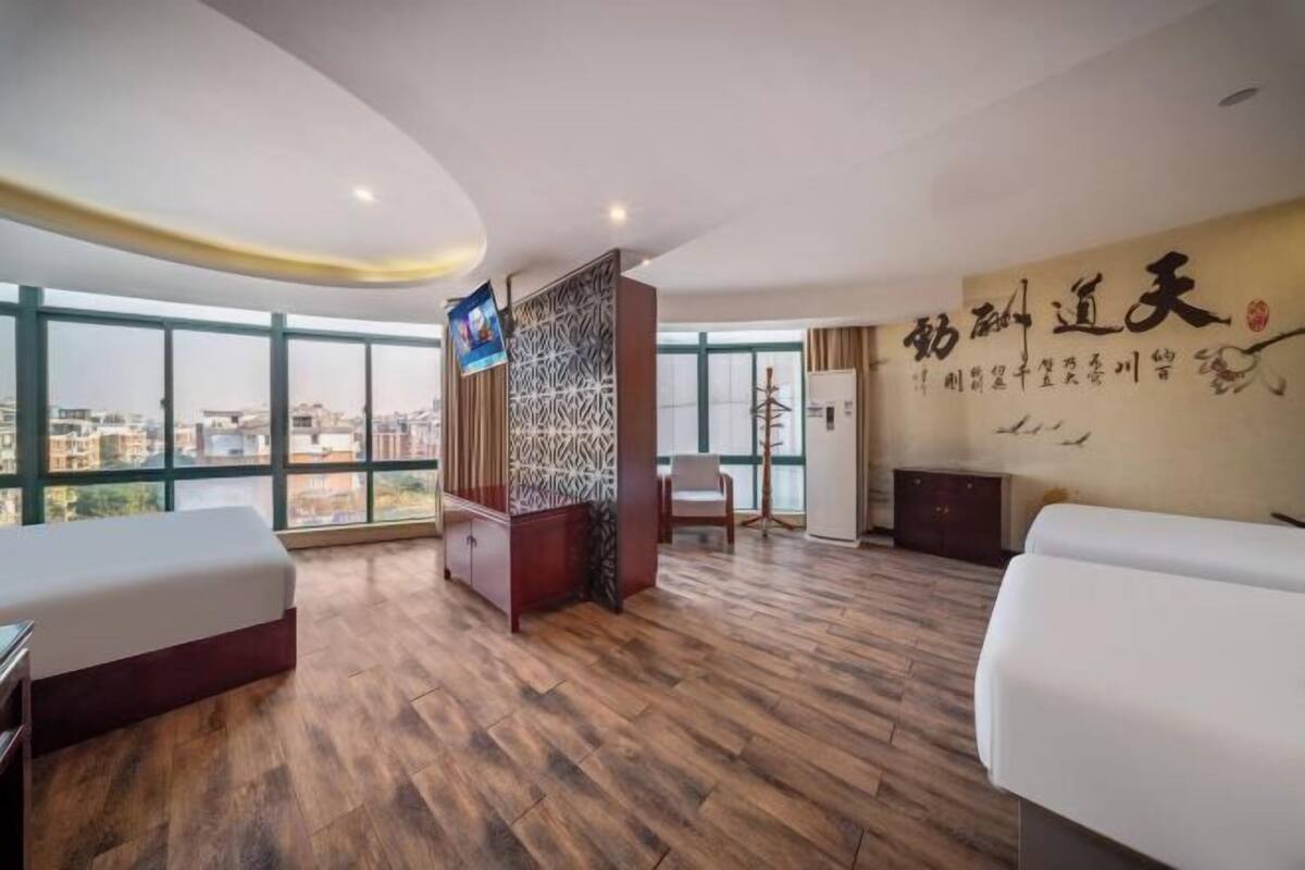 A hotel room with a large window, a wooden floor, a bed, a desk, and a TV.