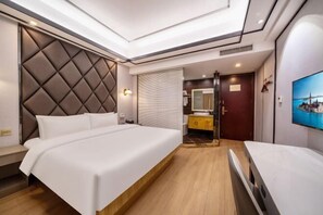 Ein Hotelzimmer mit einem großen Bett, einem Nachttisch, einem Spiegel, einem Fernseher und einem Badezimmer mit Waschbecken und Spiegel.