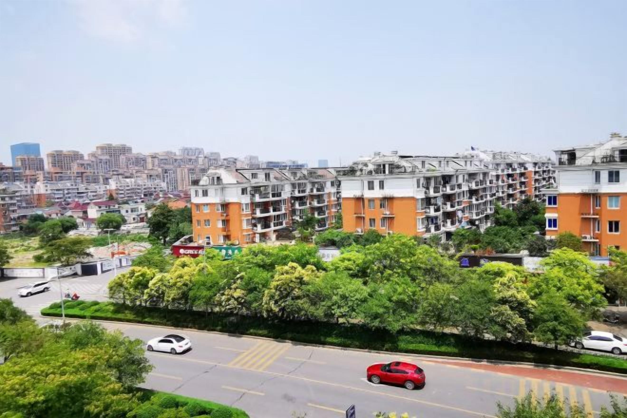 A residential area with multi-story apartment buildings, a road with vehicles, and a clear sky.