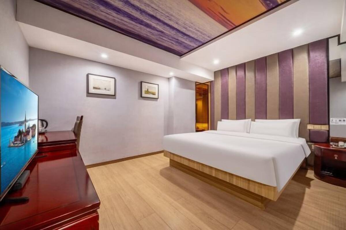 A hotel room with a large bed, a desk with a TV, and a wooden floor.