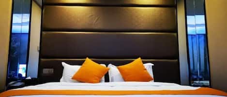 A hotel room with a large bed, a dark headboard, and two windows with curtains.