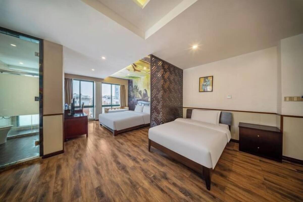 A modern hotel room with a large bed, a smaller bed, a desk, and a view of the city.