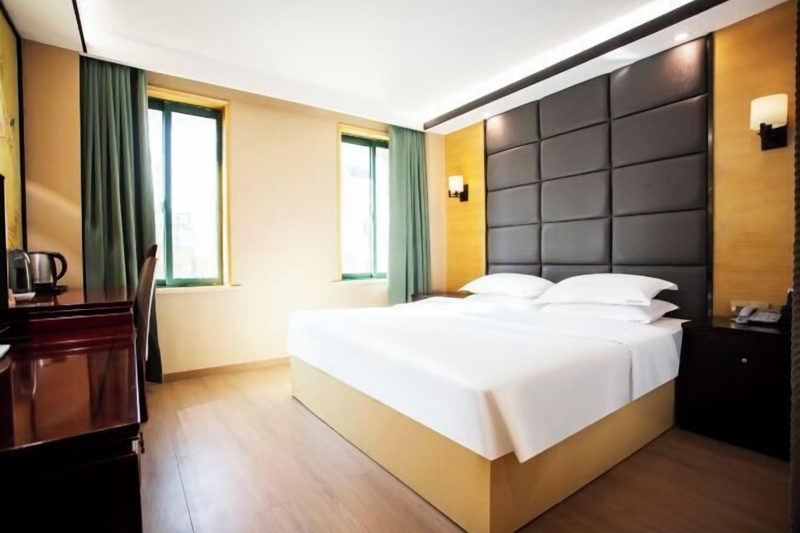 Una habitación de hotel con una cama grande, un escritorio y dos ventanas con cortinas.