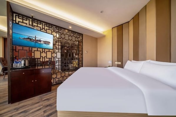 A hotel room with a large bed, a TV on a stand, a desk with a chair, and a decorative wall panel.