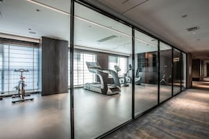 Un gimnasio moderno con equipamiento de ejercicio, ventanas amplias y un muro divisorio de vidrio.