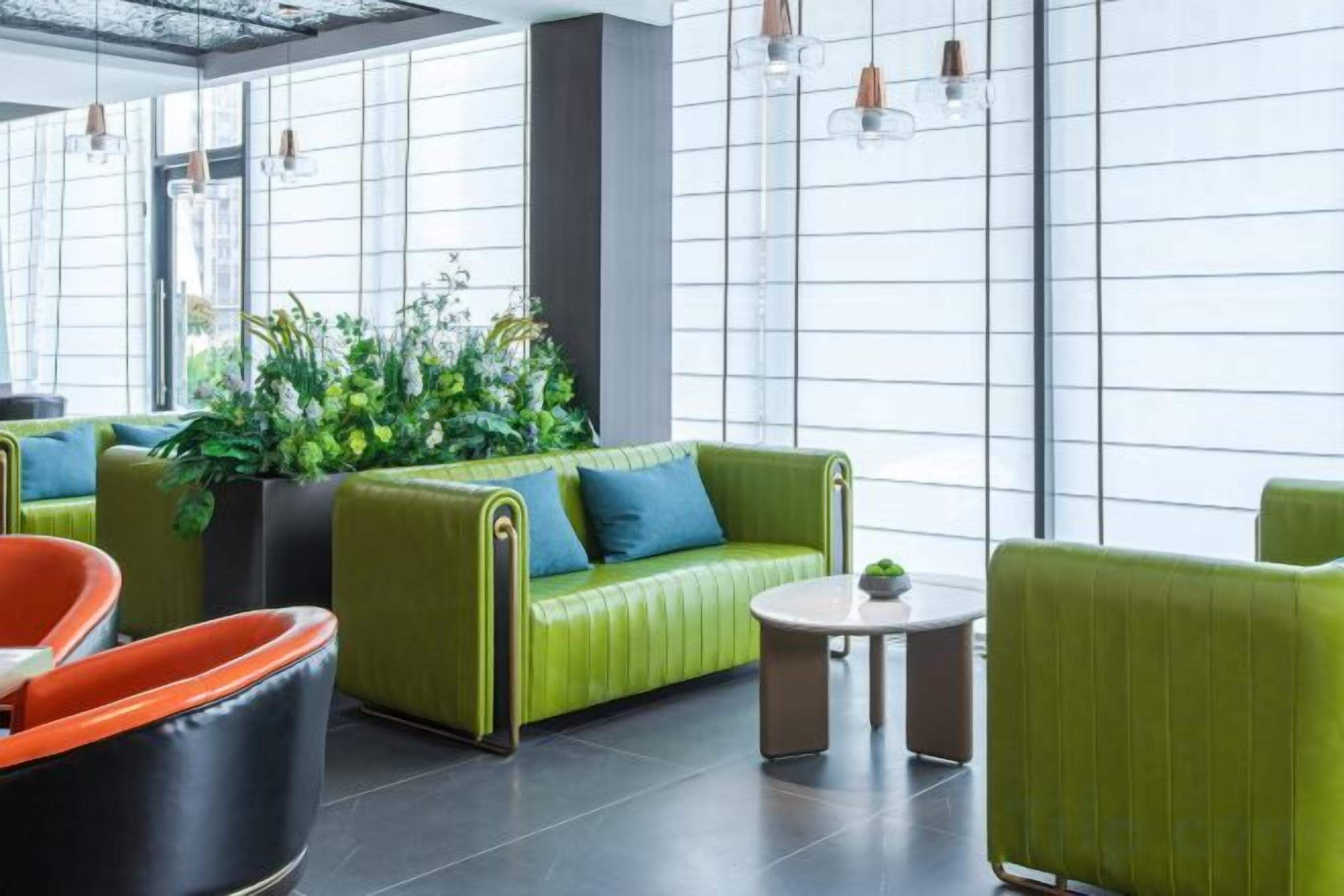 A modern lobby with green sofas, a coffee table, and a large potted plant.