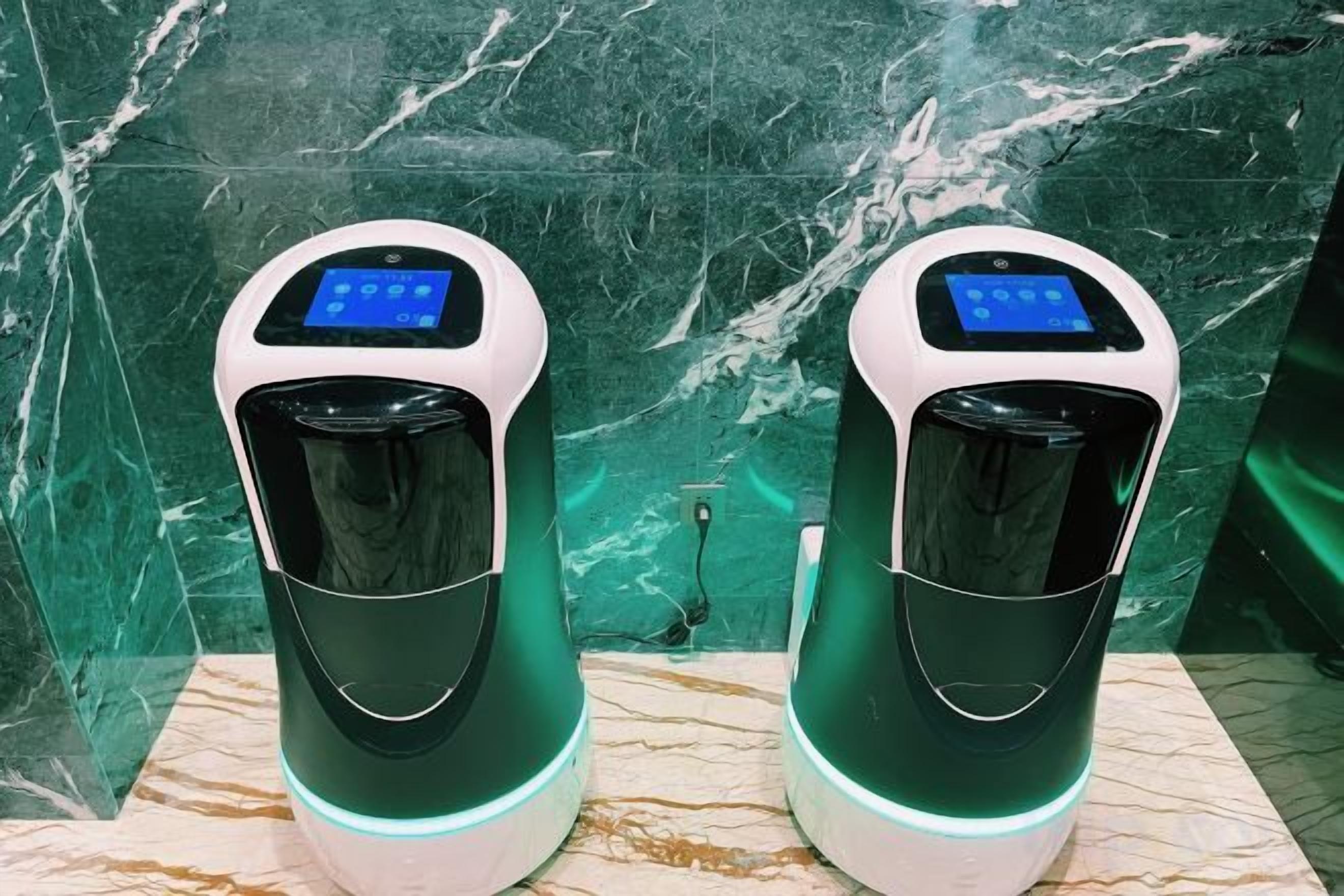 Dos máquinas expendedoras de café con pantallas digitales, sobre una superficie de mármol frente a una pared de mármol verde.