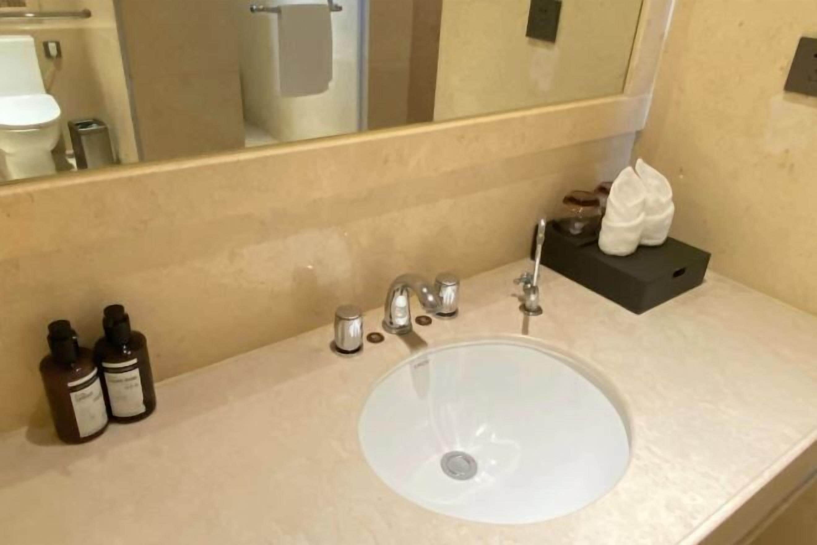 Un baño con un lavamanos blanco, un espejo y artículos de aseo en la encimera.