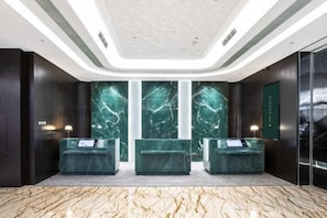 A reception area with marble walls, a reception desk, and a modern ceiling design. - Huaxin Pinyue Hotel (Hai'an)