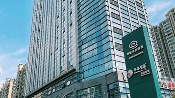 A high-rise building with a modern glass facade and a prominent green sign with white text.