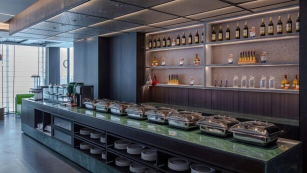 A modern bar area with a variety of bottles and glasses on shelves, buffet-style food service with trays, and a clean, contemporary design.