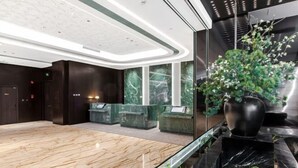 A modern lobby with a marble reception desk, a large potted plant, and a glass railing.