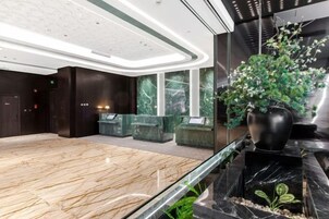 Un vestíbulo moderno con una recepción de mármol, una planta grande en maceta y una barandilla de vidrio.