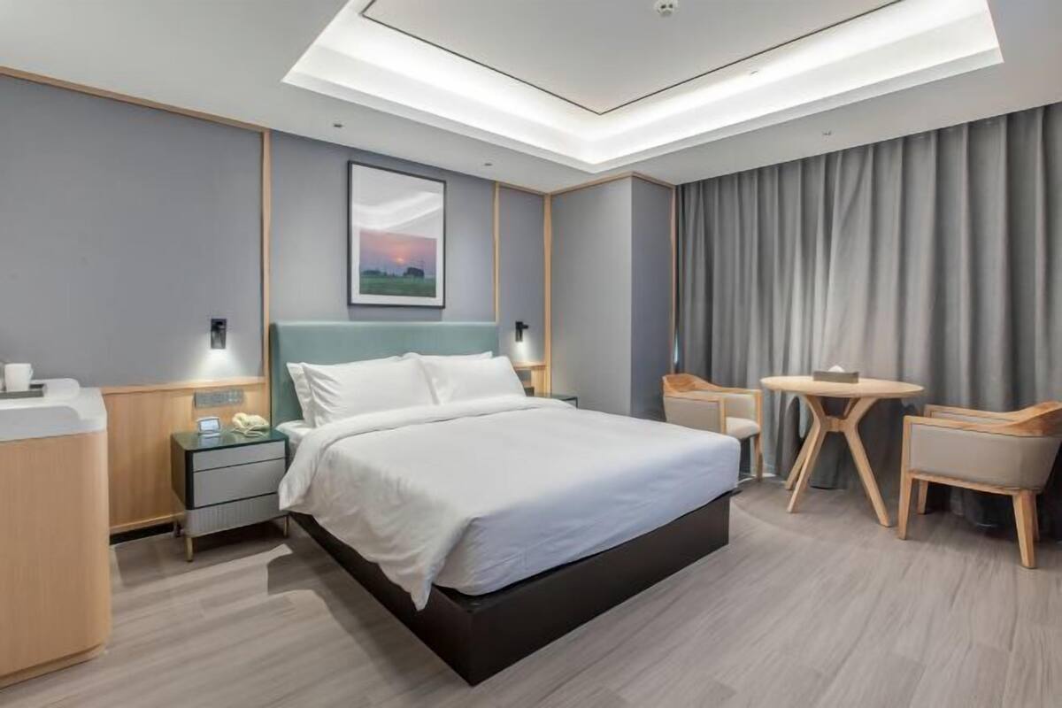 A modern hotel room with a large bed, a desk, a chair, and a small table.