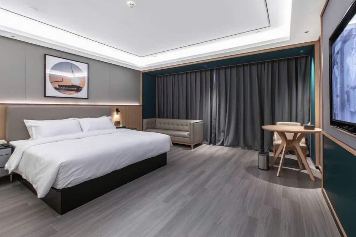 A modern hotel room with a large bed, a sofa, a small table, and a TV.