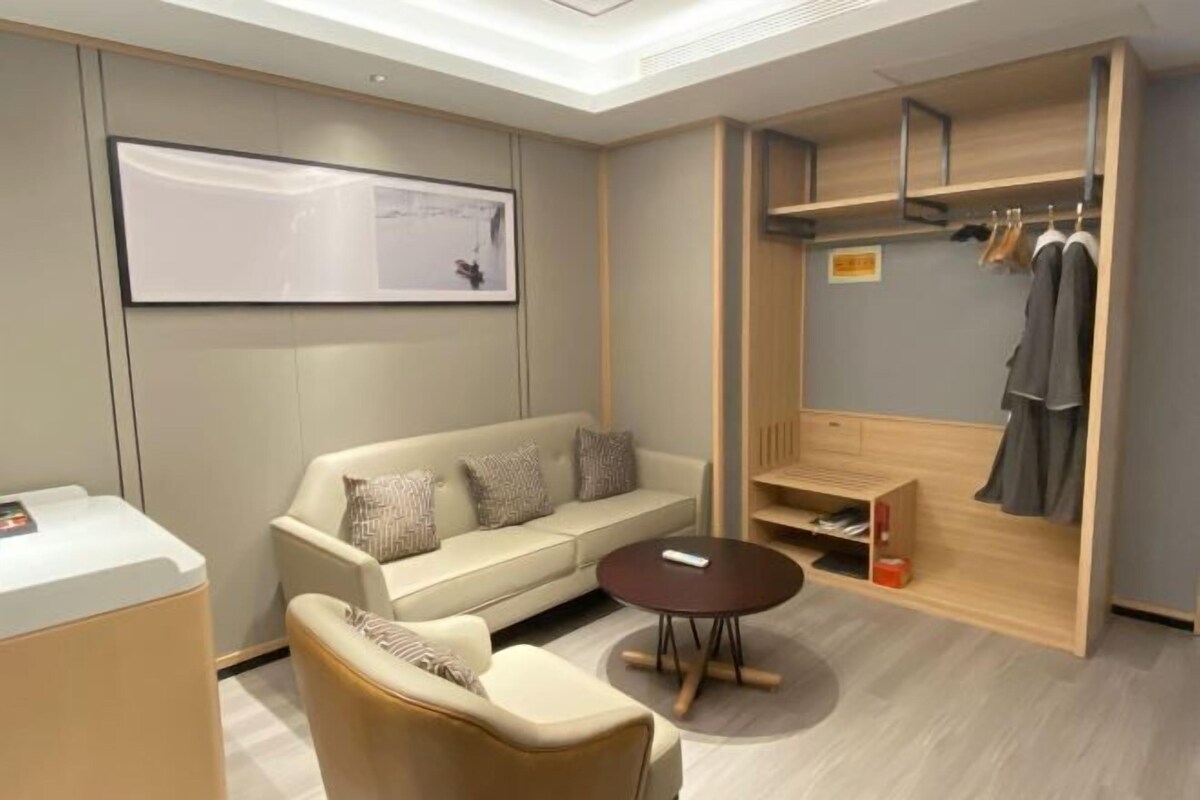 Ein modernes Hotelzimmer mit einer Couch, einem Couchtisch, einem Kleiderschrank mit Kleidung und einem gerahmten Bild an der Wand.