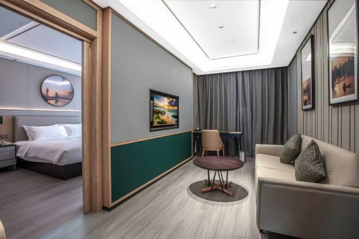 A modern hotel room with a bed, a sofa, a small table, and a painting on the wall.