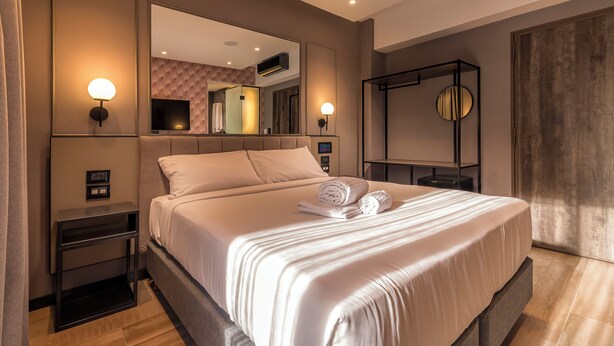 Une chambre d’hôtel moderne avec un grand lit, une table de chevet, un miroir et un climatiseur fixé au mur.