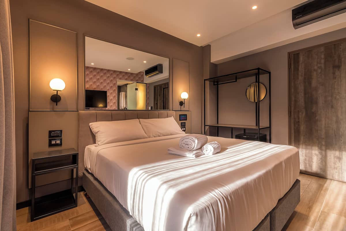 A modern hotel room with a large bed, a bedside table, a mirror, and a wall-mounted air conditioning unit.