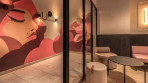Un intérieur moderne agrémenté d’une grande fresque murale, d’un espace salon avec une table ronde et d’une enseigne portant le nom « UP LA PRIDA ».