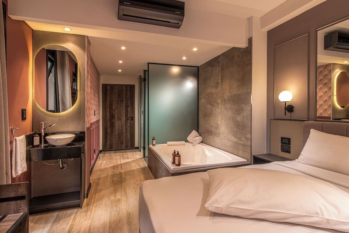 A modern hotel room with a large bed, a bathroom with a bathtub, a sink, and a mirror.