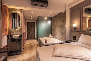 A modern hotel room with a large bed, a bathroom with a bathtub, and a vanity with a sink and mirror.
