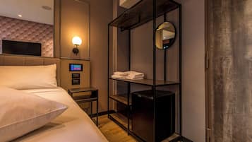 Habitación de hotel con cama, televisión, luz empotrada, estante con toallas y una mesita.