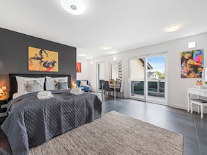 Relax in a spacious room with a large bed, desk, and sofa, surrounded by vibrant artwork and a sliding glass door leading to an outdoor area.