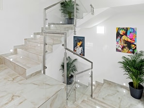 Stylish interior with a glass staircase, marble steps, and artwork adorning the walls.