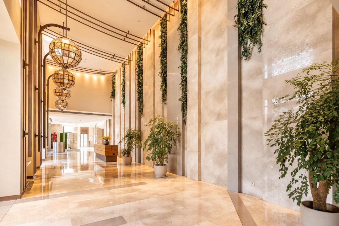 A hotel lobby with a polished marble floor, vertical greenery, and a modern chandelier.