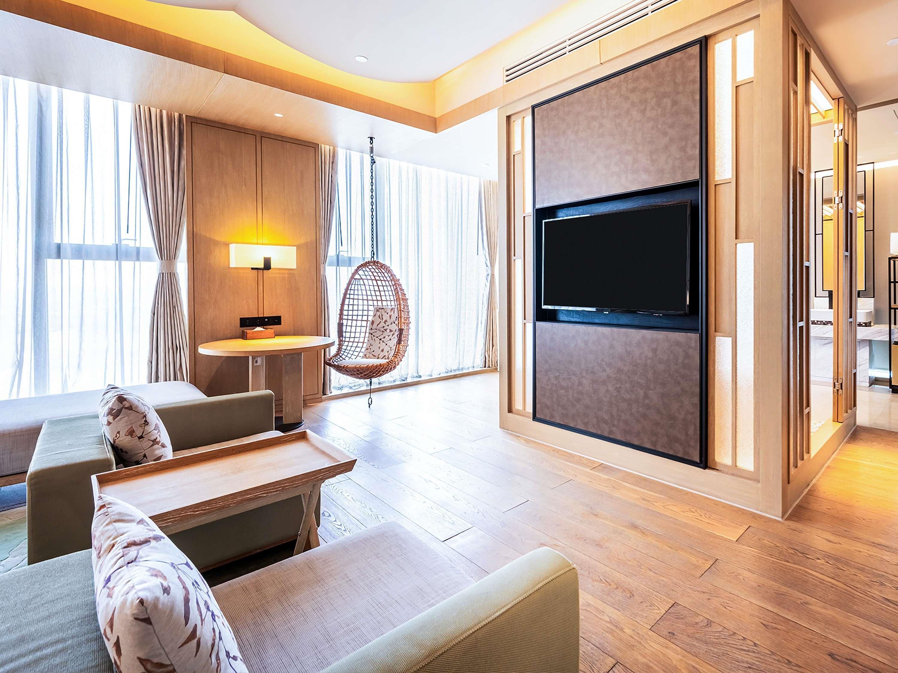 Una habitación de hotel moderna con una televisión grande, suelo de madera, un sill ón colgante y una zona de comedor.