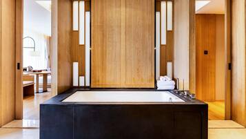 A modern bathroom with a large black bathtub, wooden panels, and a view into a living area.