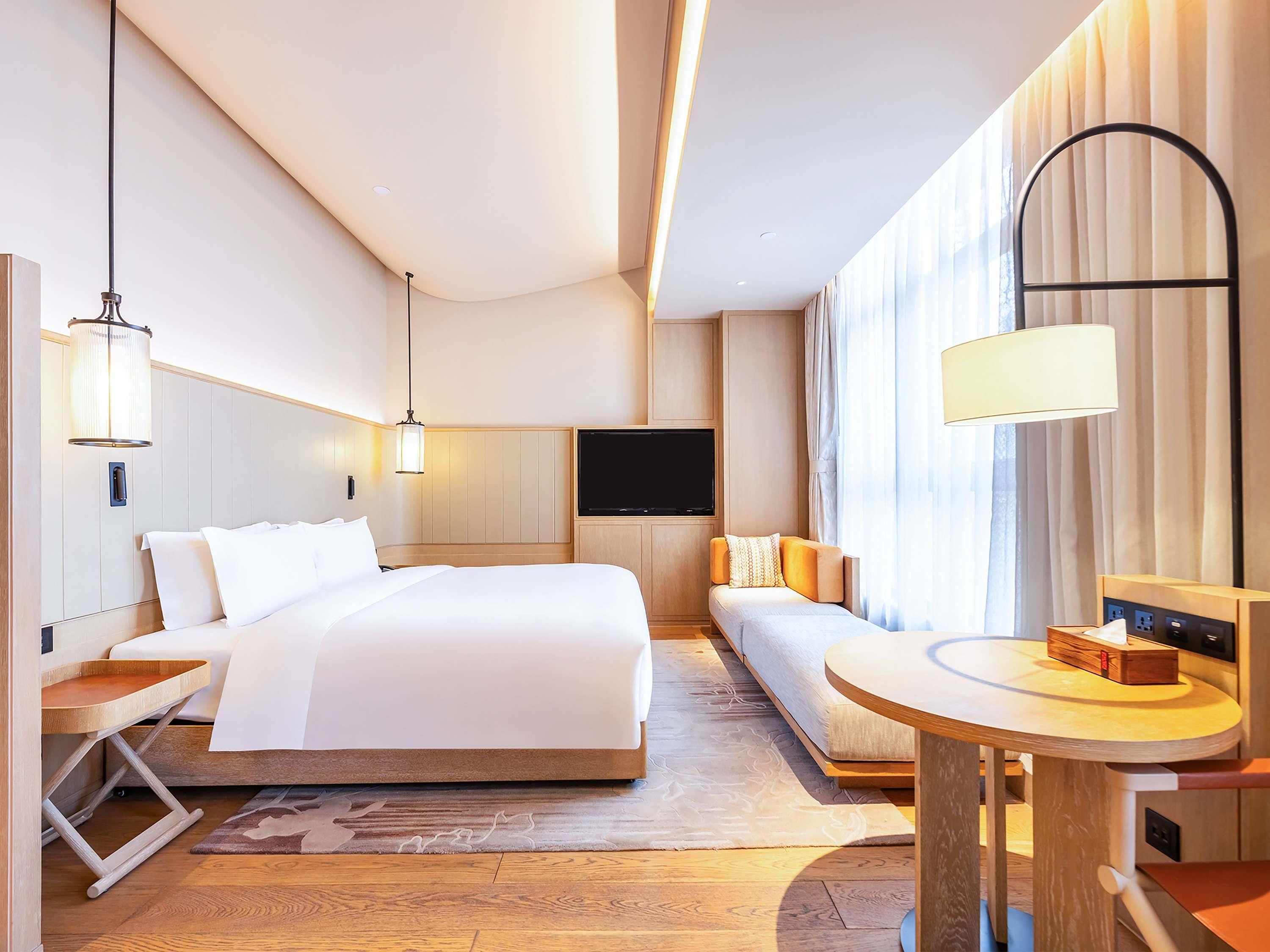 Une chambre d’hôtel moderne dotée d’un grand lit, de tables de chevet, d’un canapé, d’une télévision et d’un bureau avec une lampe.