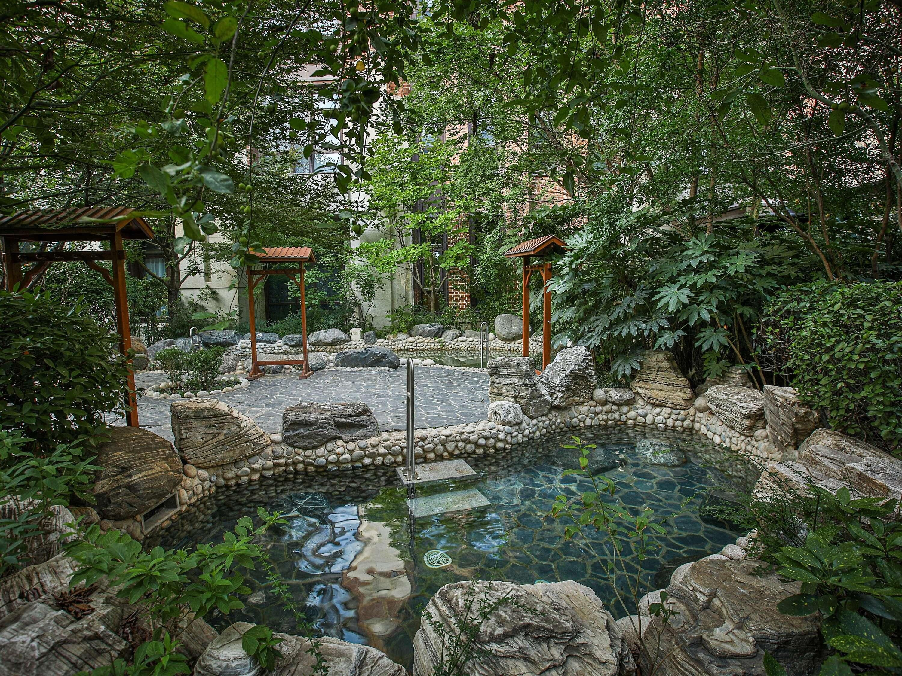 A serene garden with a stone pond, wooden pergolas, and lush greenery.