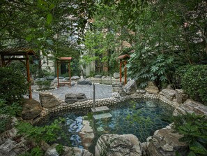 Un jardín tranquilo con un estanque de piedra, pérgolas de madera y abundante vegetación.