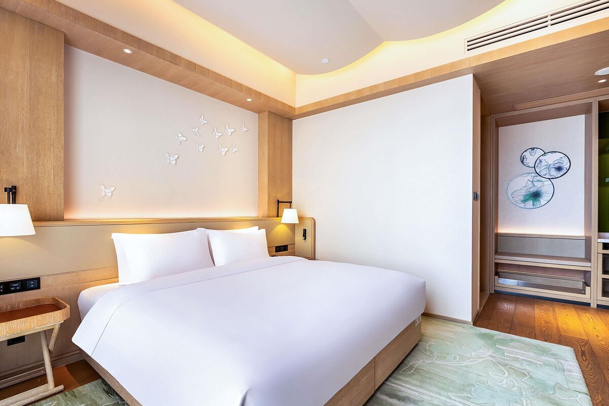 A modern hotel room with a large bed, a nightstand, a lamp, and a wall with butterfly decorations.