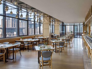 Un restaurante amplio con techos altos, ventanas grandes que ofrecen vistas de la ciudad e iluminación colgante moderna.
