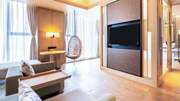 A modern hotel room with a large flat-screen TV, a hanging chair, and a sofa with a side table.