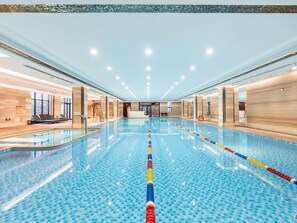A large indoor swimming pool with clear lane dividers, a lifeguard chair, and a reception area with a sign indicating the pool's location. - Swissotel Hot Spring Hotel Xi'an Xinxing (Xi'an)